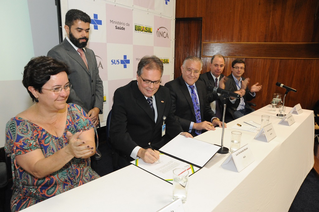 Luis Fernando Bouzas assinando o termo de posse. Do lado esquerdo dele está sentada uma mulher e do direito três homens.