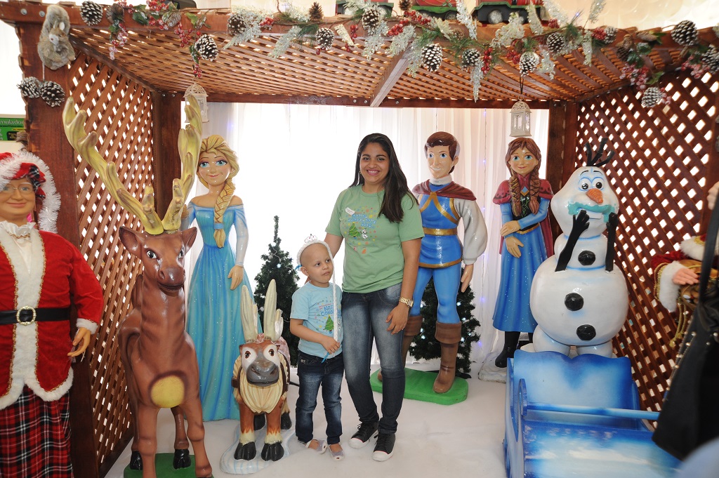Uma mulher, em pé do lado de uma criança. Ao fundo diversos personagens do filme Frozen